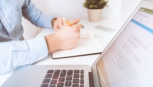 Person working at desk with laptop computer and notepad.